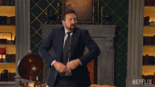 a man in a suit and tie is dancing in front of a fireplace with netflix written on the wall behind him