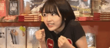 a girl in a black shirt with a red heart on it is giving a thumbs up in front of a shelf of books .