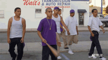 a group of young men are walking down a street in front of a walt 's transmission and auto repair shop