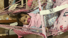 a baby with a pacifier in her mouth is sitting in a pink and white hammock