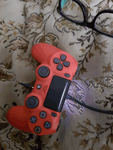 a red ps4 controller is laying on a couch next to a pair of glasses