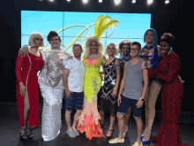 a group of drag queens pose for a photo in front of a large screen with the letter b on it