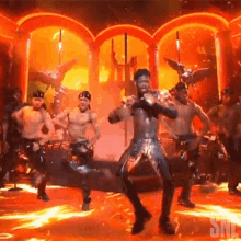 a group of men are dancing on a stage with flames coming out of the walls .