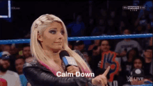 a woman in a wrestling ring is holding a microphone and says calm down