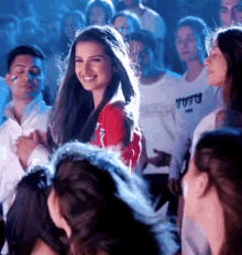 a woman in a red shirt is smiling in front of a crowd wearing a t-shirt that says ' vogue '