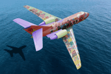 a colorful airplane is flying over the ocean with a shadow of an airplane