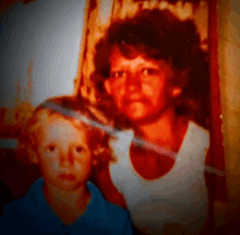 a woman in a white tank top is holding a young boy in a blue shirt