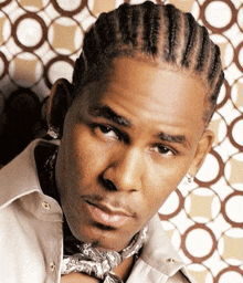 a man with braids and a scarf around his neck looks at the camera .