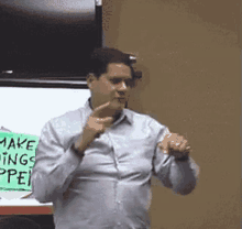 a man in a blue shirt is giving a presentation in front of a sign that says make things open .