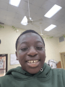 a young boy wearing a green hoodie is smiling in front of a ceiling fan