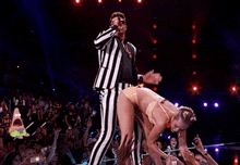 a man in a striped suit is singing into a microphone while a woman in a bikini stands on stage .