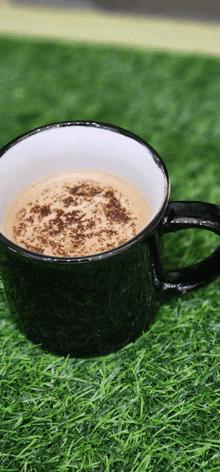 a cup of coffee with cinnamon sprinkled on top sits on the grass