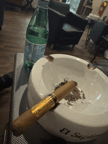 a bottle of san pellegrino water sits on a table next to an ashtray with a cigar in it