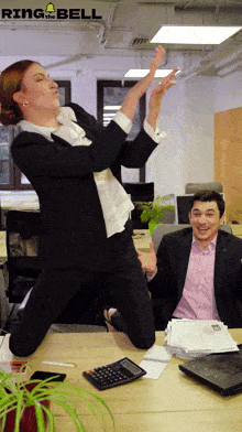 a woman is jumping in the air while a man sits at a desk with a calculator and papers on it