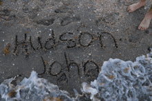 the name hudson john is written in the sand on a beach