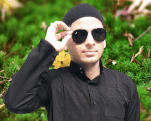 a man wearing sunglasses and a black hat stands in front of a green background