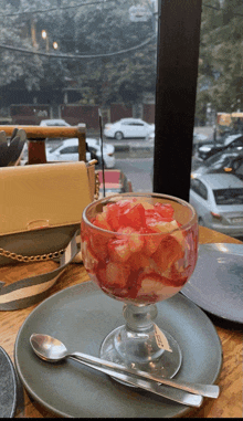 a bowl of fruit sits on a plate with a spoon on a table