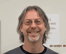 a man with glasses and a beard smiles in front of a sign that says stand and walk