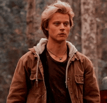 a young man wearing a brown jacket and a necklace .