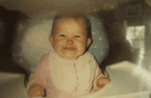 a baby in a high chair with a bib on looks at the camera