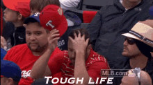 a group of people are sitting in a stadium and one of them is wearing a red hat that says t on it .