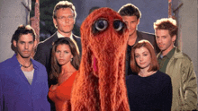 a group of people standing next to each other with a red monster in the middle