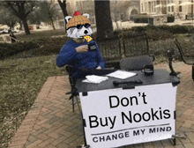 a man sitting at a table with a sign that says do n't buy nookis