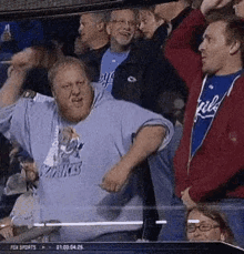 a group of men are sitting in a stadium watching a baseball game and one of them is making a funny face .