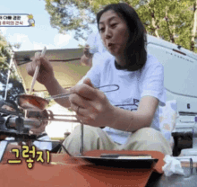 a woman is sitting at a table with a plate of food and chopsticks in front of a foreign language sign