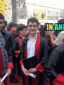 a boy in a graduation cap and gown holds a diploma in front of a sign that says " in ani "