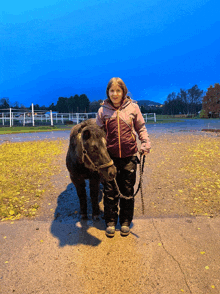 a girl is standing next to a small black animal on a leash