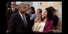 a man in a suit and tie is standing next to a woman holding a baby in front of a wall that says comedy central