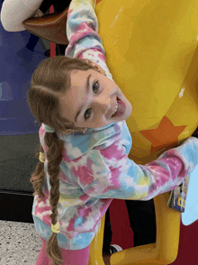 a little girl wearing a tie dye sweatshirt is standing next to a statue of mickey mouse