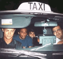 a group of men are sitting in a taxi with a sign above them that says taxi