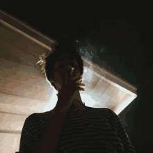 a man in a striped shirt is smoking a cigarette in a dark room