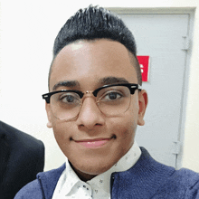 a young man wearing glasses and a blue jacket smiles