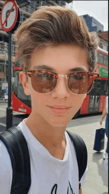 a young man wearing sunglasses and a backpack is taking a selfie on a street .