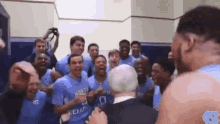 a group of basketball players are posing for a picture in a locker room with a man in a suit .