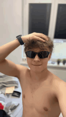 a shirtless young man wearing sunglasses holds his hand to his forehead