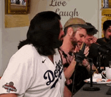 a group of men are sitting in front of a microphone . one of the men is wearing a dodgers jersey .