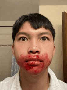 a young man has blood on his face and looks at the camera