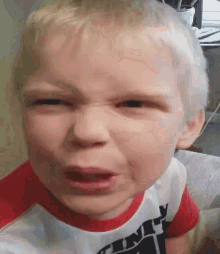 a young boy is making a funny face with his mouth open while wearing a red and white shirt .