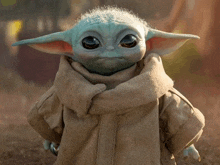 a baby yoda from star wars is standing in the dirt wearing a brown coat and scarf .