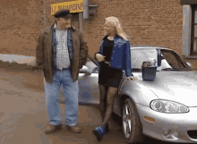 a man and a woman are standing next to a silver car in front of a building that says lc de kampioene