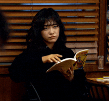 a woman sitting in front of a window reading a book that says ' samurai ' on the cover