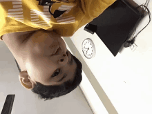 a young boy in a yellow shirt is upside down in front of a wall clock that shows the time as 4:20