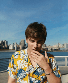 a young man wearing a yellow and blue floral shirt covering his mouth