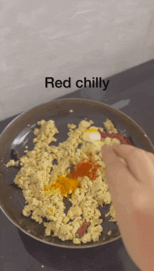 a person is adding red chilly to a frying pan of food