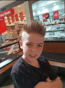 a young boy with a mohawk stands in front of a sign that says 50 % off shoes