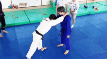 a man in a white karate uniform is wrestling another man in a blue karate uniform on a blue mat .